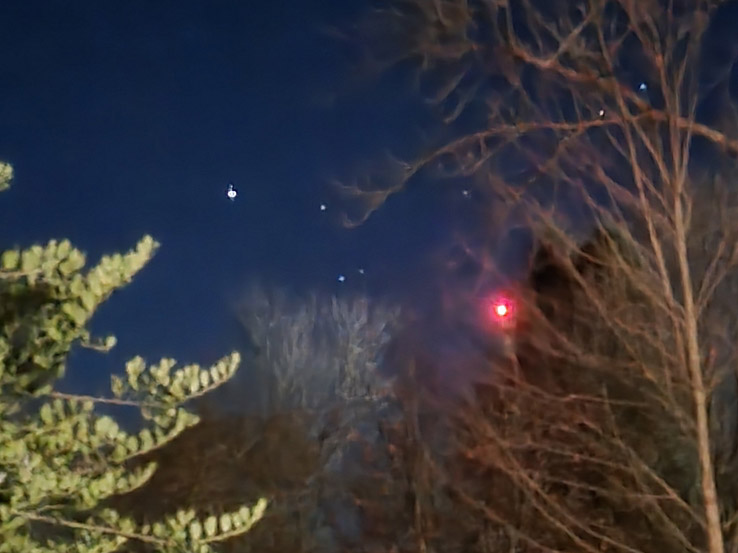 Brilon 2024 - bemannter Gasballon Helles rotes Licht am Himmel, das sich nahe oder hinter einigen Bäumen zeigt.
