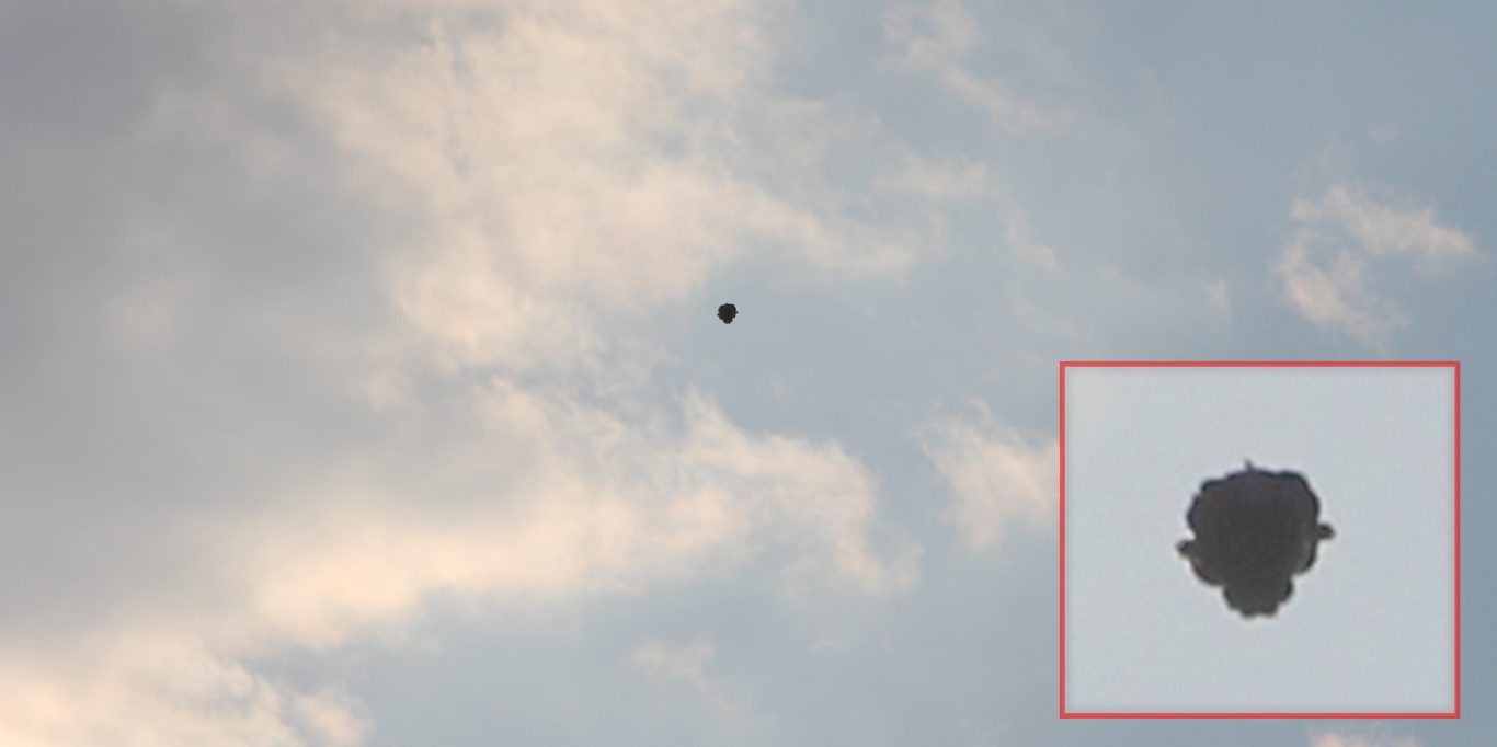 Derendingen 2015 - Wahrscheinlich Folienballon Am teilbewölkten Himmel ein dunkles Objekt, das außen herum Ausbuchtungen aufweist und ein käferförmiges Aussehen aufweist.